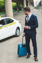 handsome man with suitcase and smartphone looking at taxi cab