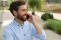 Handsome man talking on phone outdoors, space for text Royalty Free Stock Photo