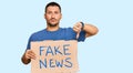 Handsome man with tattoos holding fake news banner with angry face, negative sign showing dislike with thumbs down, rejection