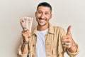 Handsome man with tattoos holding 10 united kingdom pounds banknotes smiling happy and positive, thumb up doing excellent and