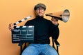 Handsome man with tattoos holding video film clapboard and louder relaxed with serious expression on face