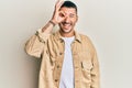 Handsome man with tattoos wearing casual brown denim jacket doing ok gesture with hand smiling, eye looking through fingers with Royalty Free Stock Photo