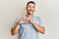 Handsome man with tattoos wearing casual 90s style and gold chain smiling in love doing heart symbol shape with hands Royalty Free Stock Photo