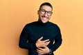 Handsome man with tattoos wearing turtleneck sweater and glasses smiling and laughing hard out loud because funny crazy joke with Royalty Free Stock Photo