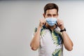 Handsome man touches medical mask in quarantine covid-19 period. Man weared t-shirt isolated white background Royalty Free Stock Photo