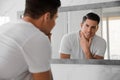 Handsome man touching his smooth face after shaving near mirror in bathroom Royalty Free Stock Photo