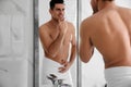 Handsome man touching his smooth face after shaving near mirror in bathroom Royalty Free Stock Photo