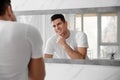 Handsome man touching his smooth face after shaving near mirror in bathroom Royalty Free Stock Photo