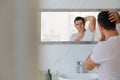 Handsome man touching his smooth face after shaving near mirror in bathroom Royalty Free Stock Photo