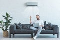 handsome man turning on air conditioner with remote control while using laptop on sofa Royalty Free Stock Photo