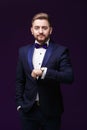 Handsome man in tuxedo and bow tie looks at watch. Fashionable, festive clothing. emcee on dark background Royalty Free Stock Photo
