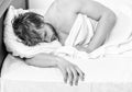 Handsome man using clock in bed after waking up in the morning. Picture showing young man stretching in bed. Royalty Free Stock Photo