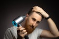 Handsome man is using hairdryer for his hairstyle on grey background Royalty Free Stock Photo