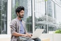 Handsome man using laptop in a city. Smiling indian male student working on computer outdoor Royalty Free Stock Photo