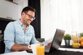 Handsome man using laptop computer at home, drinking juice and coffee in the morning. Royalty Free Stock Photo