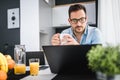 Handsome man using laptop computer at home, drinking juice and coffee in the morning. Royalty Free Stock Photo