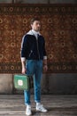 handsome man with vintage little suitcase in front of rug hanging