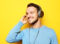 Handsome man wearing blue sweater and headphones and holding mobile phone over yellow background Royalty Free Stock Photo