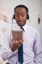 Handsome man wearing headphones with microphone, white striped shirt and tie, posing holding tablet in hand, smiling Royalty Free Stock Photo