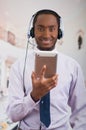 Handsome man wearing headphones with microphone, white striped shirt and tie, posing holding tablet in hand, smiling Royalty Free Stock Photo