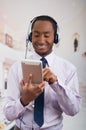 Handsome man wearing headphones with microphone, white striped shirt and tie, posing holding tablet in hand, smiling Royalty Free Stock Photo