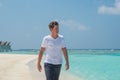 Handsome man wearing white t-shirt and black shorts walking on the tropical beach at the island luxury resort