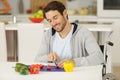 Handsome man in wheelchair cuts pepers with knife Royalty Free Stock Photo