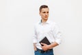 Handsome man in a white shirt with a notebook near a white wall.