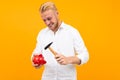 Handsome man in a white shirt smashes a piggy bank with a hammer on a yellow background Royalty Free Stock Photo