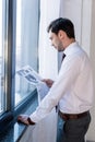 Handsome man in white shirt standing by window and business reading newspaper.