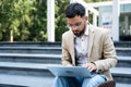 Handsome man working on laptop in city street. Man using his knowledge while sitting on stairs outdoors. Businessman successful Royalty Free Stock Photo