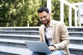 Handsome man working on laptop in city street. Man using his knowledge while sitting on stairs outdoors. Businessman successful Royalty Free Stock Photo