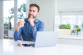 Handsome man working using computer laptop and drinking a cup of coffee serious face thinking about question, very confused idea Royalty Free Stock Photo