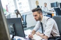 Handsome man writing notes on a writing pad while sitting at his desk in front of computer in office. Royalty Free Stock Photo