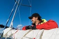 Handsome man on yacht touches white sail called assymetric spinnaker, works with tackle in sea at summer day, under view