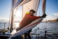 Handsome man on yacht touches white sail called assymetric spinnaker, works with tackle in sea at summer day, under view