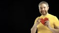 Handsome man in yellow tshirt holds red heart shape. Love, romance, dating, relationship concepts. Black background Royalty Free Stock Photo