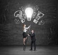 A handsome manager assists a beautiful colleague to climb up the stairs to reach new business ideas. A light bulb as a concept of Royalty Free Stock Photo