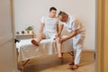 Handsome masseur therapist in white uniform making manual therapy for young athlete knee. Professional massage treatment