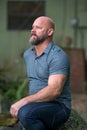 Handsome mature bald man with gray beard sitting looking away from camera