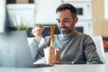 Handsome mature business man eating take away noodles while working with laptop at home Royalty Free Stock Photo