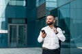 Handsome mature businessman browsing net on cellphone during coffee break, walking near office, copy space