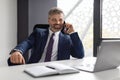 Handsome Mature Businessman Sitting At Workplace In Office And Talking On Cellphone Royalty Free Stock Photo