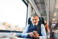 Mature businessman with smartphone travelling by train. Royalty Free Stock Photo