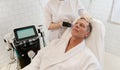 Handsome mature European man in white terry robe receiving facial mesotherapy treatment in modern wellness spa center. Hardware
