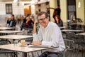 Smiling attractive stylish mature man using smart phone checking online sitting outside coffee shop Royalty Free Stock Photo