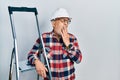 Handsome mature handyman close to construction stairs wearing hardhat bored yawning tired covering mouth with hand
