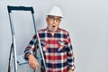 Handsome mature handyman close to construction stairs wearing hardhat in shock face, looking skeptical and sarcastic, surprised Royalty Free Stock Photo