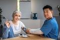 Handsome mature korean man doctor measures pressure with tonometer to senior female, patient waving hand