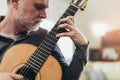 Mature man in casual clothes is smiling while playing guitar at home Royalty Free Stock Photo